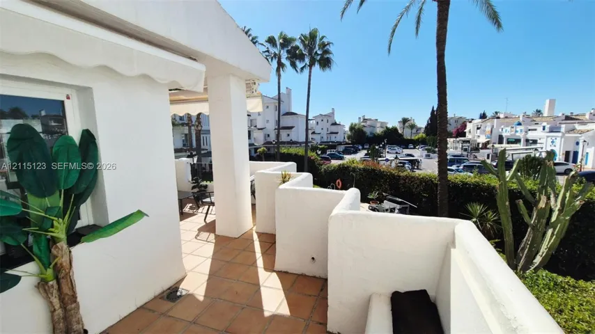 Covered terrace featuring terra cotta tile flooring, white stucco walls, and built-in masonry seating