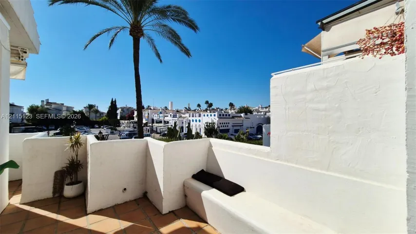Terrace featuring stucco walls, built-in bench seating, terracotta-style tile flooring, and a palm tree