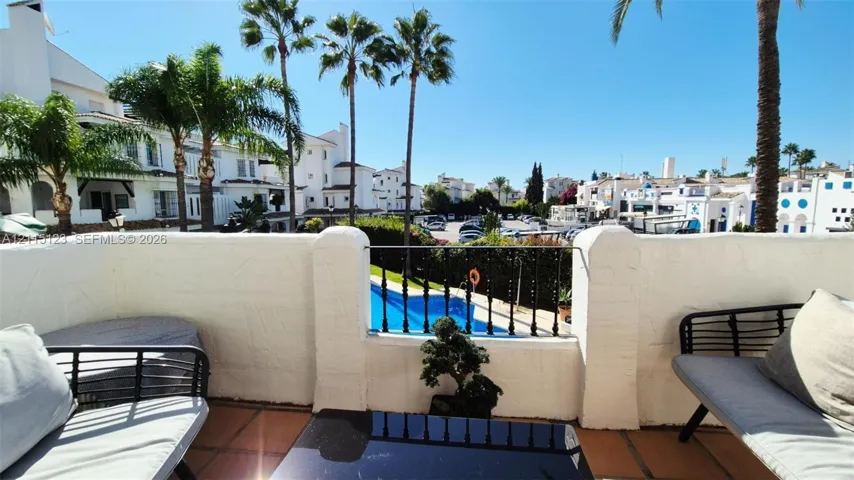 Covered balcony featuring a terracotta tile floor, stucco masonry walls, and a decorative wrought iron railing overlooking a swimming pool