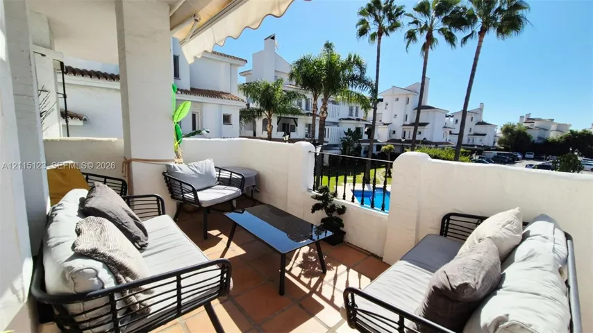 Covered balcony featuring terracotta tile flooring, stucco privacy walls, retractable awning, and metal railing