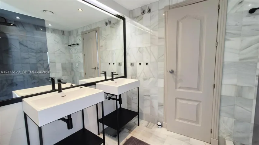 Dual rectangular wall-mounted sinks with matte black hardware, stone-tiled wall surfaces, and a large framed mirror