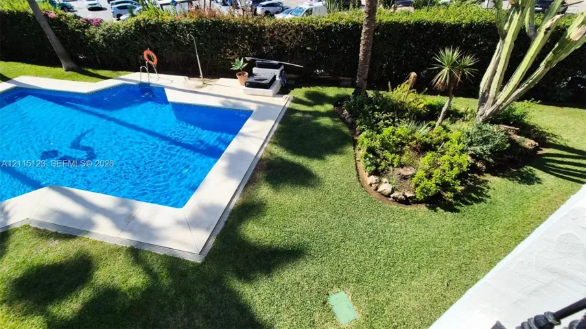 In-ground swimming pool with stone coping, manicured lawn, established garden beds, and mature palm trees
