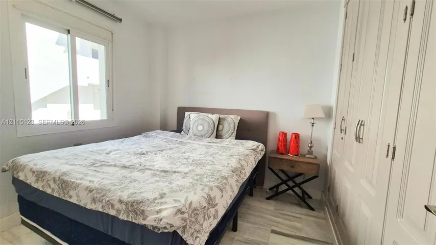 Room featuring floor-to-ceiling built-in wardrobes, neutral stone-finish flooring, and a sliding window