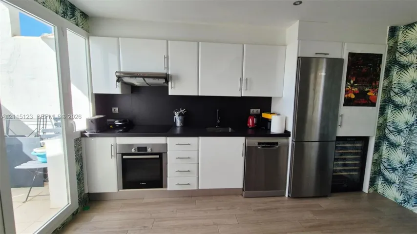 Kitchen featuring high-gloss white cabinetry, contrasting dark countertops, stainless steel appliances, a built-in wine cooler, and wood-finish flooring