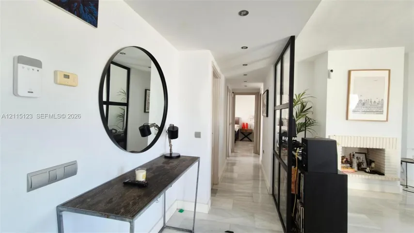 Hallway featuring stone-finish tile flooring, recessed ceiling lighting, a floor-to-ceiling metal-framed glass partition, and a fireplace with brick-style detailing