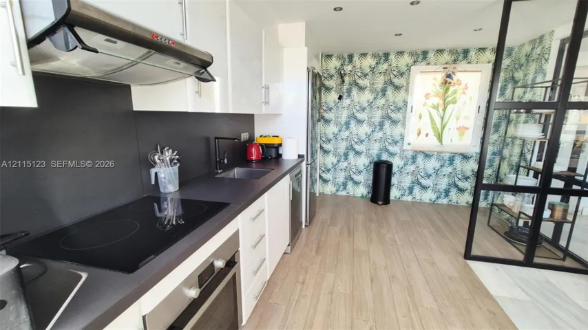 Kitchen featuring high-gloss cabinetry, matte black hardware, integrated cooktop with overhead ventilation, and a structured black-frame glass partition