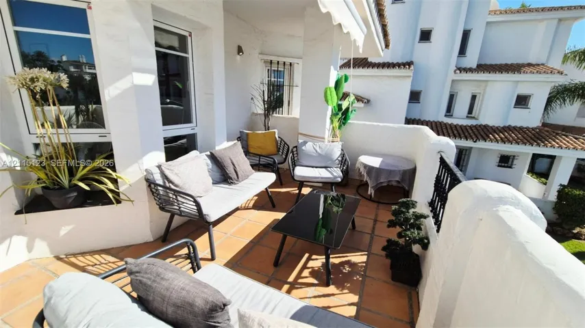 Covered terrace featuring terra-cotta tile flooring, white stucco walls, and a decorative black metal railing