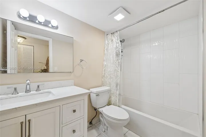 Bathroom featuring a vanity with a light-toned countertop, integrated rectangular sink, wall-mounted mirror, polished chrome lighting, and a bathtub with white vertical-stacked wall tile