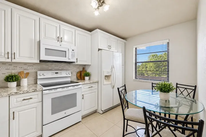 Kitchen featuring white cabinetry, stone-finish countertops, tile backsplash, white appliances, and ceramic tile flooring