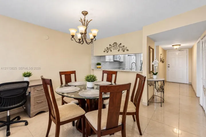 Neutral tile flooring, decorative multi-arm chandelier, and open-concept pass-through window with solid-surface countertop