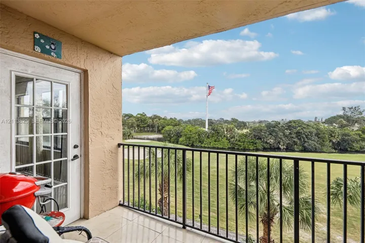 Covered balcony featuring tile flooring and a black metal railing overlooking a golf course with mature palm trees