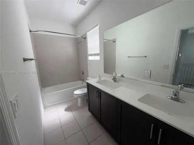 Bathroom featuring a dark-finish dual-sink vanity with white countertops, large wall-mounted mirror, ceramic tile flooring, and a bathtub with tile surround
