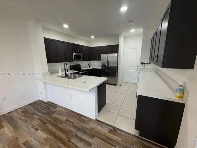Kitchen featuring dark cabinetry, stone-finish countertops, stainless steel appliances, recessed lighting, and a combination of wood-finish and tile flooring