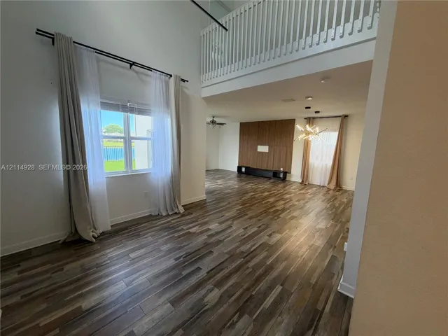 Double-height ceiling, wood-finish flooring, built-in wooden wall paneling, and a balcony with a white railing