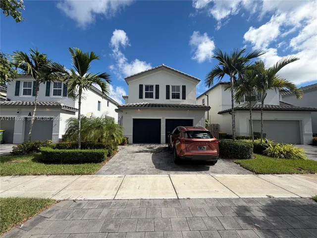 Two-story stucco exterior with a tiled roof, paver driveway, and a two-car garage
