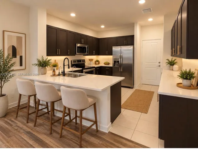 Kitchen featuring dark cabinetry, stone-finish countertops, stainless steel appliances, a center island with a built-in undermount sink, and recessed lighting