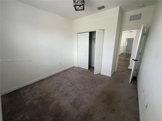 Room featuring neutral wall tones, plush carpeting, a closet with double-panel doors, and an overhead geometric metal light fixture