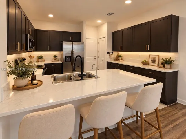 Kitchen featuring dark cabinetry, expansive quartz countertops, an undermount double-basin sink with a matte black faucet, integrated under-cabinet lighting, and wood-finish flooring