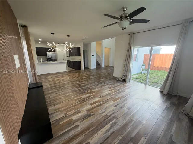 Wood-finish flooring throughout, kitchen featuring dark cabinetry and a peninsula, modern geometric pendant lighting, ceiling fan, and sliding glass doors