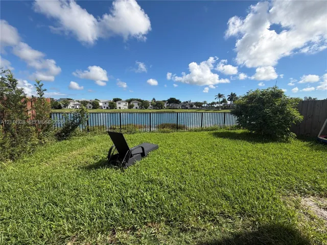 Backyard featuring a grass lawn, metal perimeter fencing, and water frontage