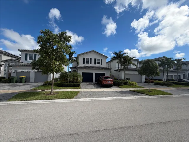 Two-story exterior featuring a tile roof, paved driveway, two-car garage, and manicured landscaping