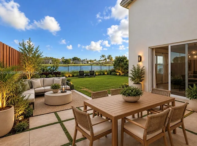 Rear patio featuring large-format pavers with grass inlay, manicured lawn, perimeter metal fencing, and wall-mounted exterior lighting