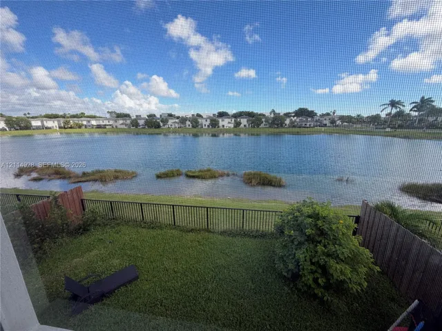 Waterfront property featuring a grass lawn, perimeter metal fencing, and wood-paneled privacy partitions