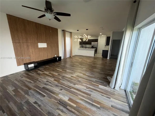 Open-concept interior featuring wood-finish flooring, a decorative vertical slat accent wall, a built-in low-profile media console, modern multi-arm light fixtures, and a ceiling fan