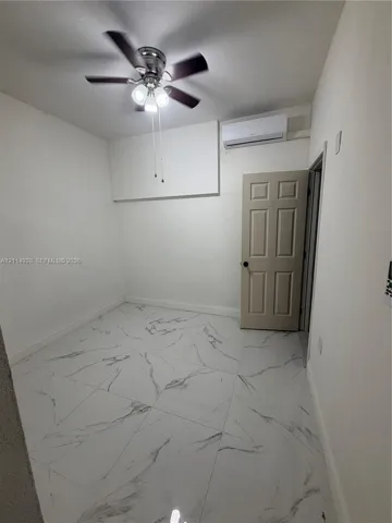 Large-format tile flooring featuring a marble-style pattern, ceiling fan with integrated lighting, and wall-mounted ductless climate control unit
