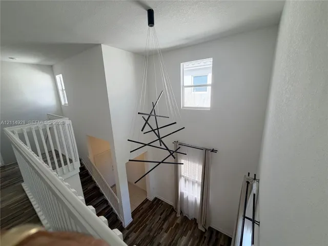 Two-story foyer featuring high ceilings, wood-finish flooring, a contemporary geometric multi-light chandelier, and white wooden balustrades
