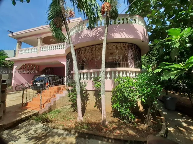 Two-story exterior featuring a curved facade, upper-level balcony with balustrade, decorative metal security screens, and an attached covered parking area