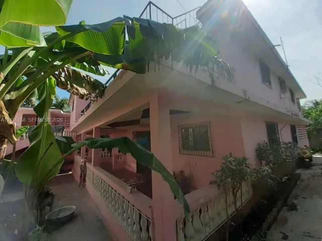 Two-story residence featuring a covered ground-level porch with decorative balustrade, upper-level terrace, and metal security bars on exterior windows