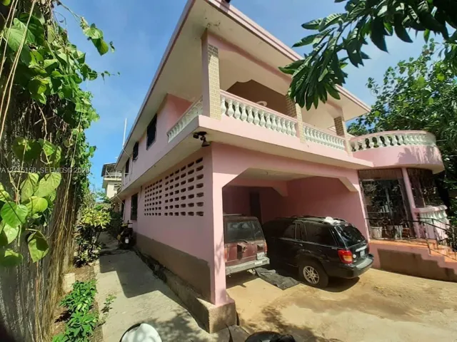 Two-story exterior featuring a covered carport, second-level balcony with concrete balustrades, decorative masonry ventilation blocks, and exterior staircase