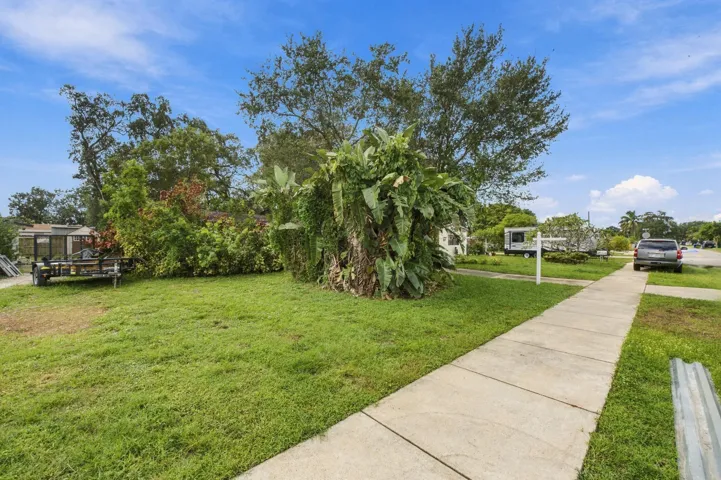 Expansive corner lot featuring mature tropical landscaping, established trees, and a concrete sidewalk