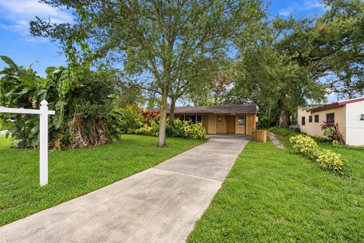 Single-story residence featuring a concrete driveway, mature canopy trees, and established ornamental landscaping