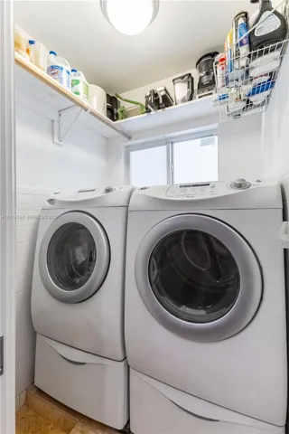 Laundry area featuring white subway tile wall cladding, fixed upper wood shelving, an operable window, and a flush-mount ceiling light fixture