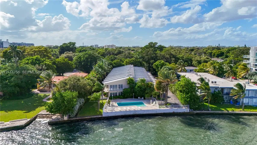 Waterfront property featuring a concrete seawall, in-ground swimming pool, paved patio, and mature landscaping