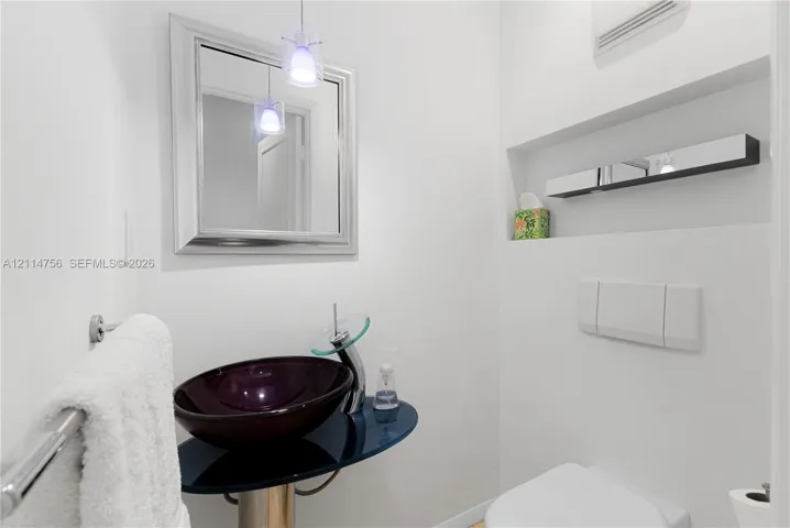 Floating vanity with a dark-tinted glass countertop, circular vessel sink, chrome-finish faucet, wall-mounted mirror, and recessed wall shelving