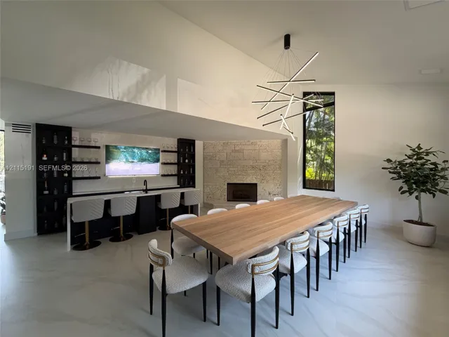 Built-in wet bar with dark cabinetry, floating shelving, and integrated sink, stone-faced fireplace, modern geometric chandelier, and large-format flooring