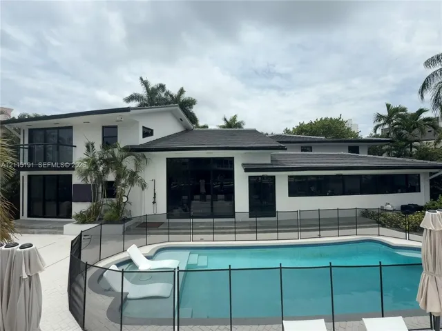Modern exterior featuring a two-story design with a flat roof, large glass sliding doors, a second-level balcony, and a swimming pool with integrated sun shelf