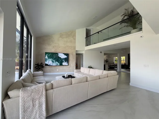 Double-height ceiling, textured accent wall, floor-to-ceiling windows, porcelain tile flooring, and glass-paneled interior railing