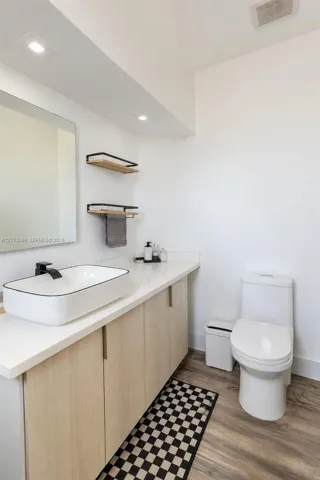 Light-toned cabinetry with a white countertop, vessel sink, matte black faucet, wall-mounted shelving, and wood-finish flooring