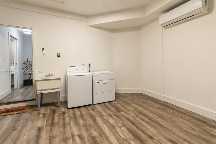 Utility space featuring wood-finish flooring, a wall-mounted ductless climate control unit, and a built-in utility sink