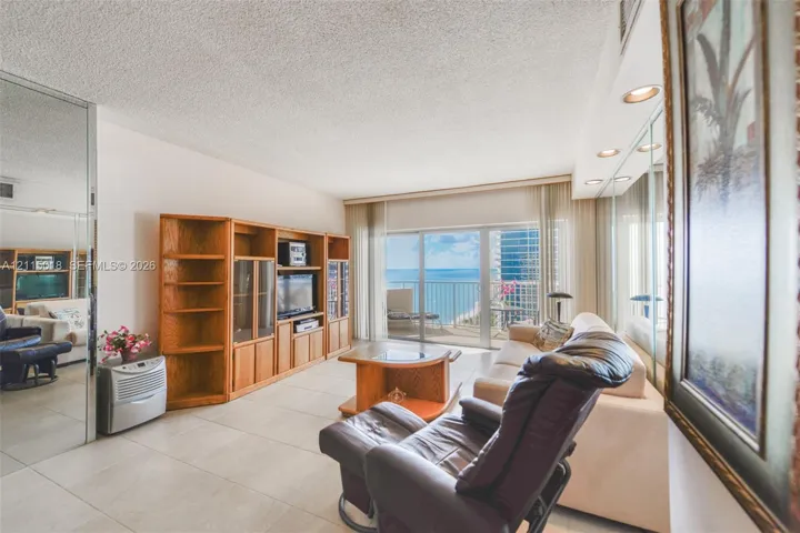 Large-format tile flooring, built-in wooden cabinetry, recessed ceiling lighting, wall-to-wall mirrored paneling, and sliding glass doors opening to a balcony
