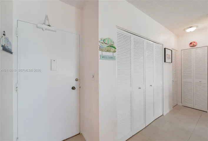 Solid core entry door with overhead hydraulic closer, louvered bi-fold closet doors, and ceramic tile flooring