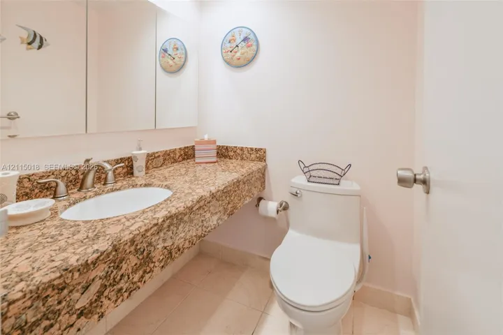 Neutral stone countertop with an integrated oval sink, brushed nickel faucet, wall-spanning triple-panel mirror, and tile flooring