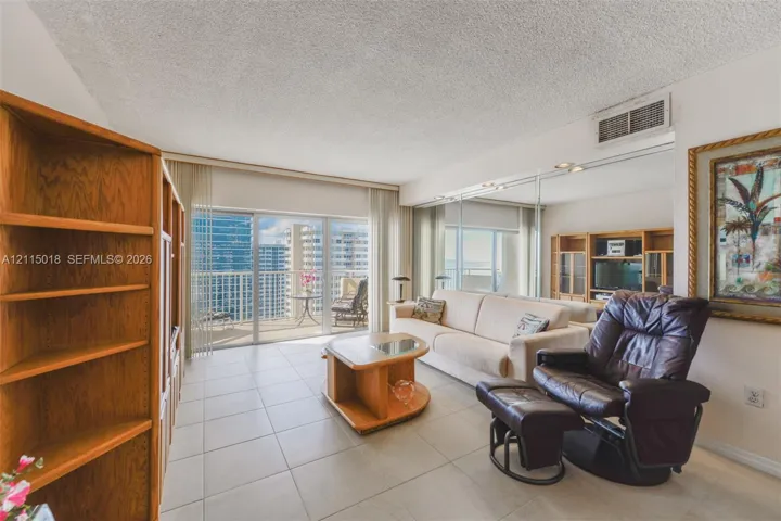 Large-format tile flooring, mirrored wall accents, built-in wooden shelving, and floor-to-ceiling glass doors opening to a balcony