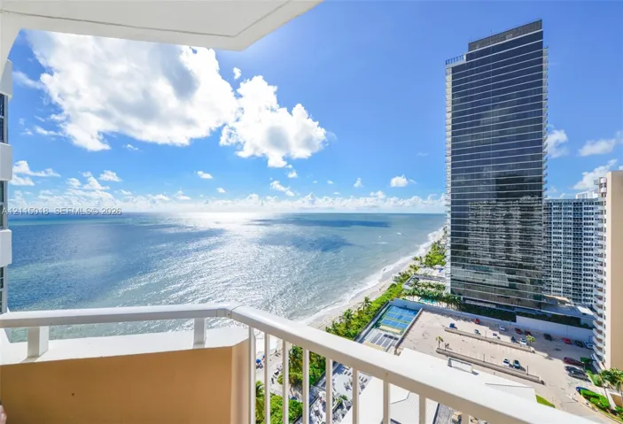 Private balcony with white metal railings overlooking the ocean shoreline and high-rise cityscape