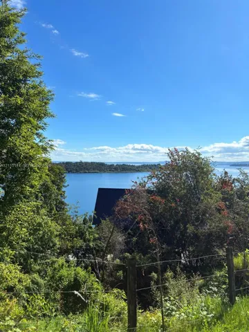 Waterfront landscape featuring mature trees, expansive lake backdrop, and wire-fence perimeter
