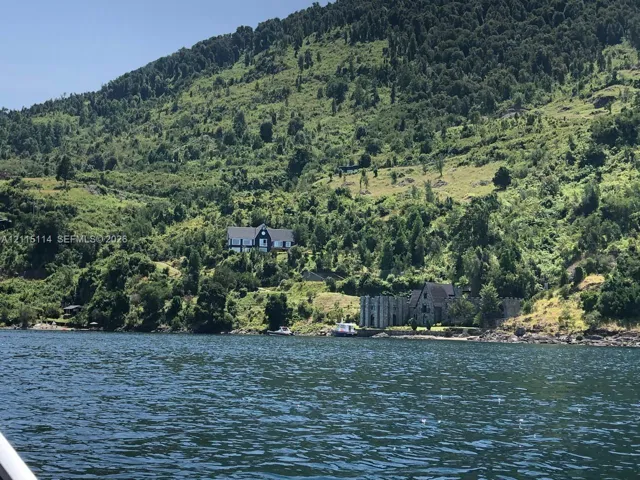 Waterfront property featuring stone-exterior architecture, a steep-pitched gable roof, and a stone retaining wall against a backdrop of forested terrain